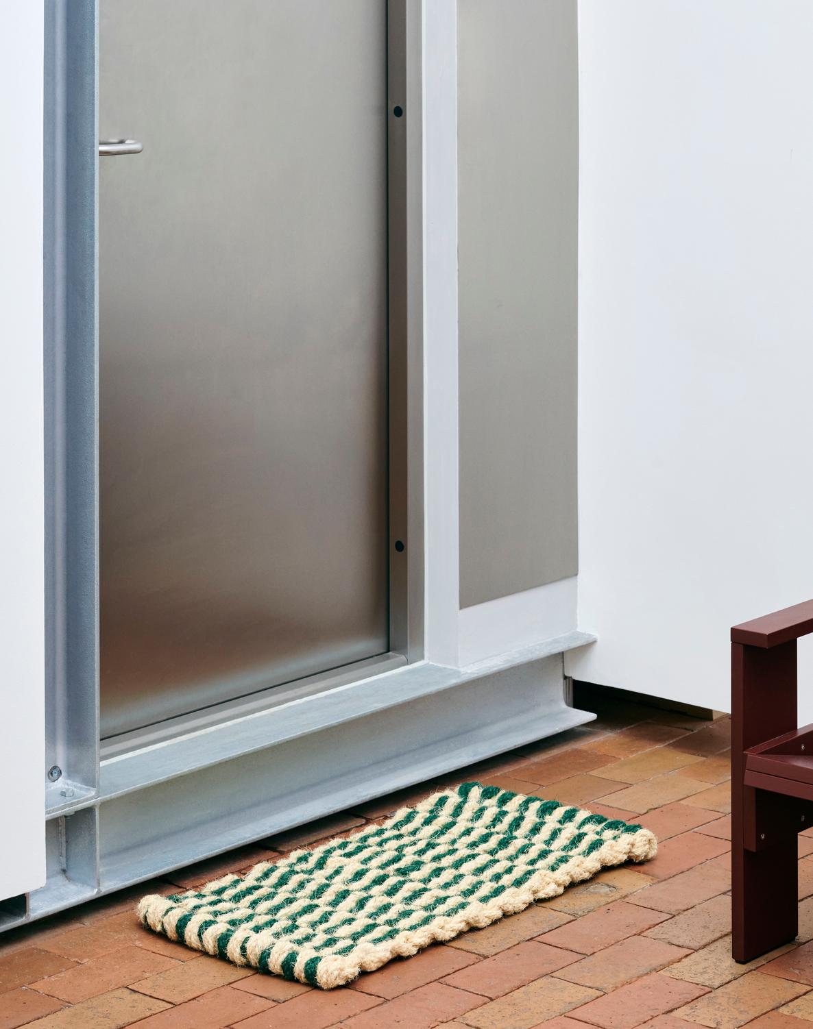 Doormat with green and white pattern on a wooden floor in front of a glass door.