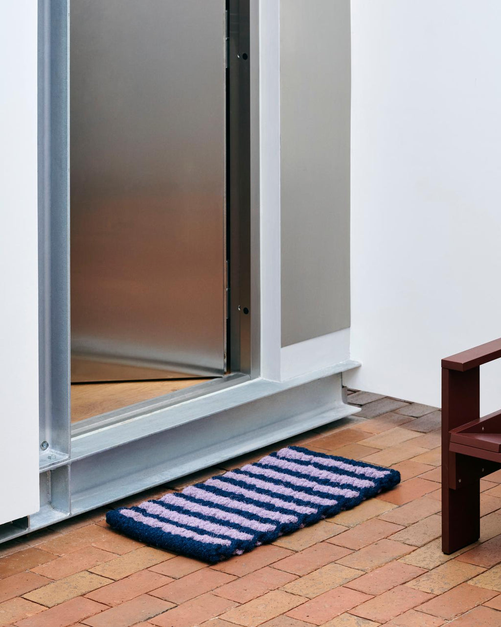 Doormat with striped pattern in front of a glass door on a brick floor.