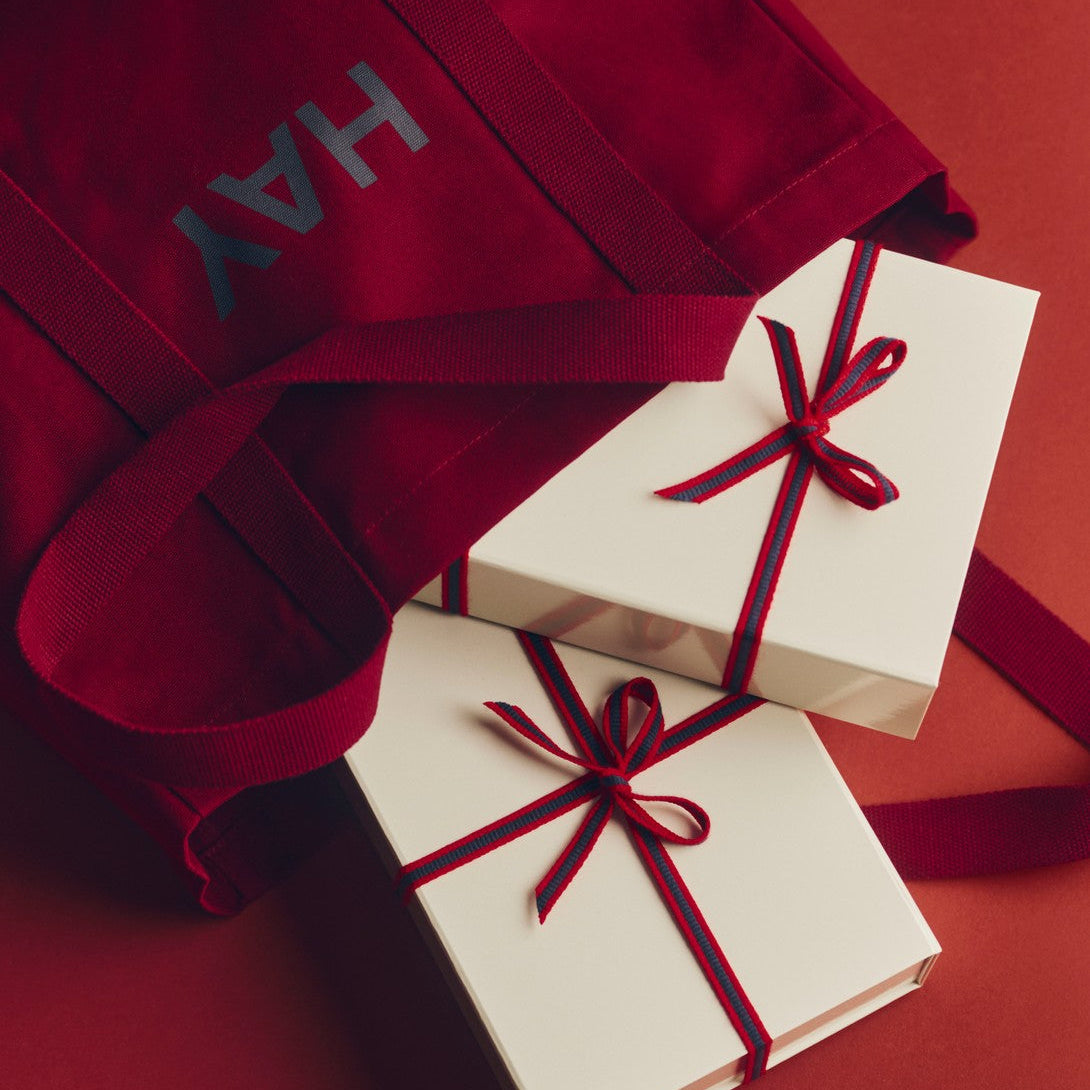 Red bag with 'HAY' branding and two wrapped gifts on a red background