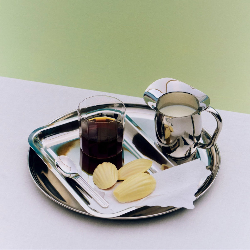 Silver tray with a glass of dark liquid, cookies, and a teacup on a light green background