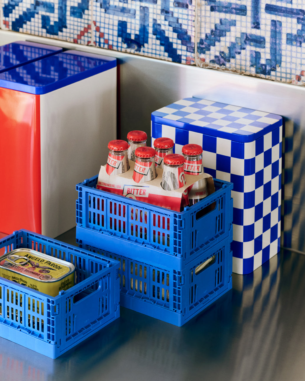 Blue crates with food items against a colorful tiled wall.
