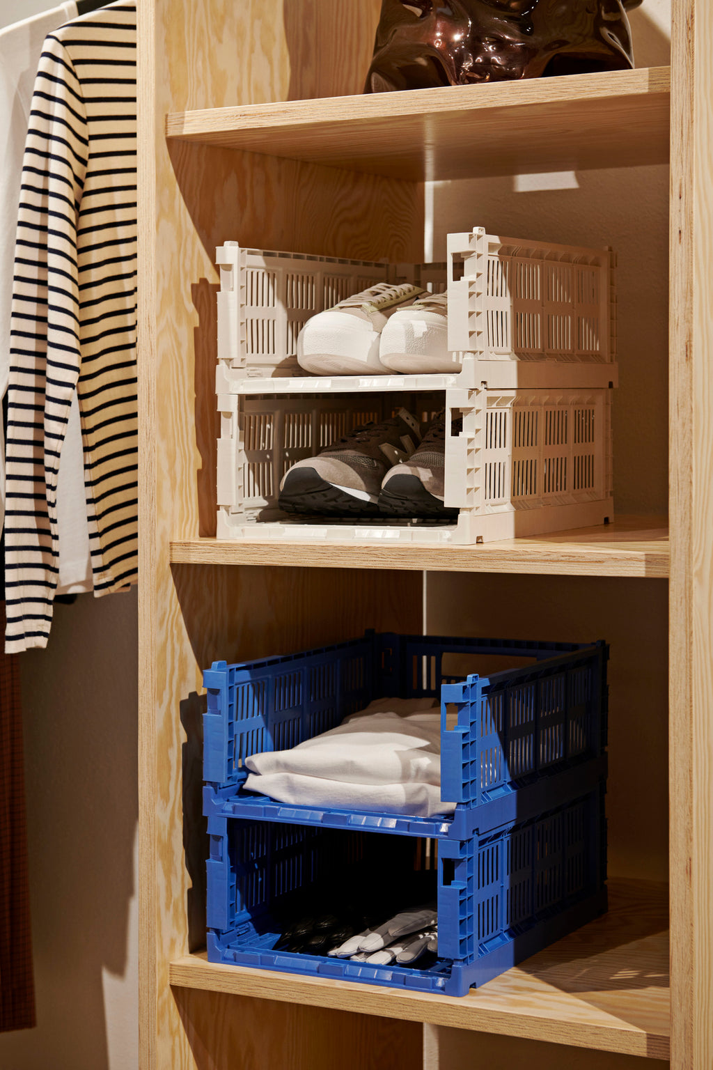 Wooden shelf with stacked plastic crates containing folded clothes.