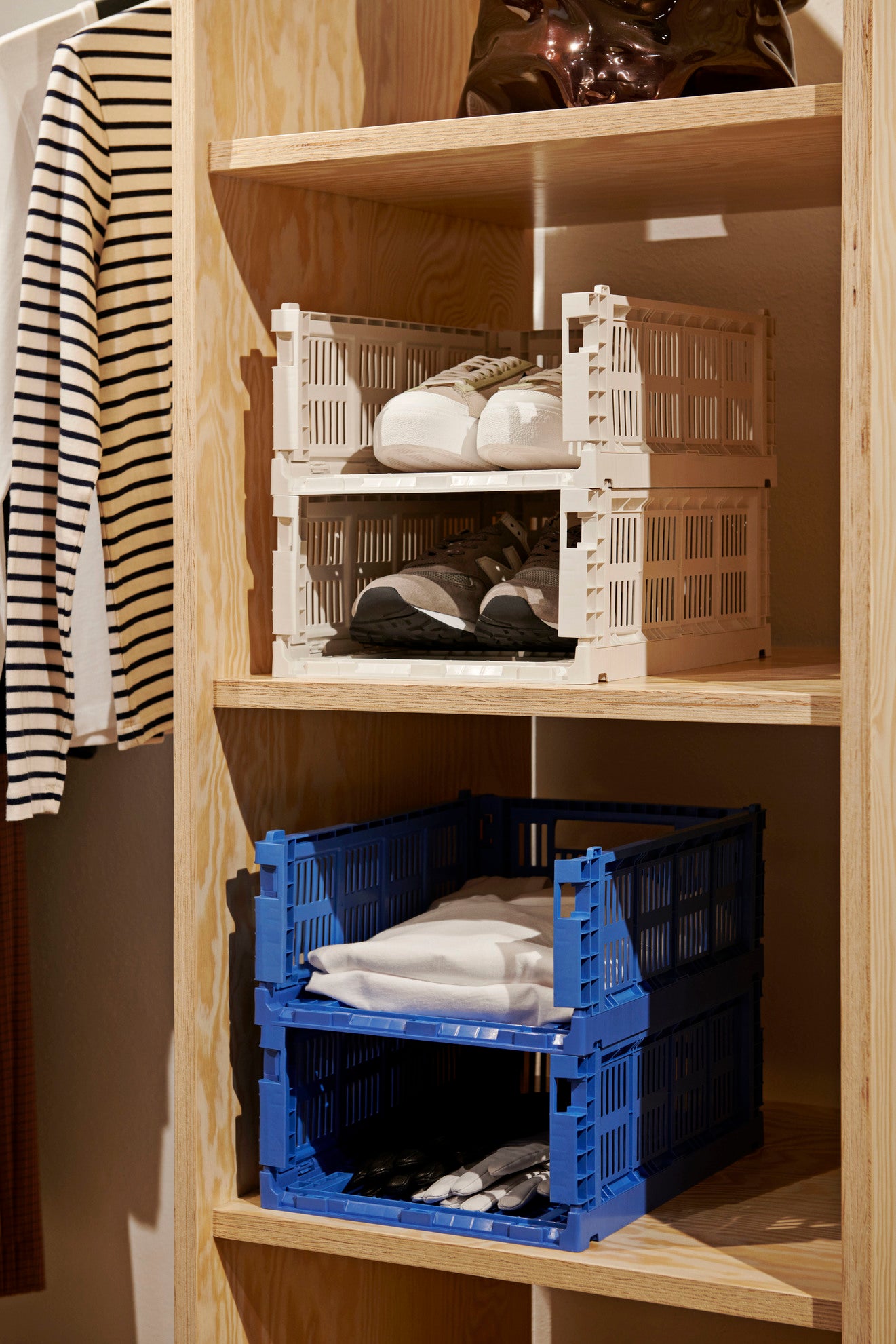Wooden shelf with stacked plastic crates containing folded clothes.