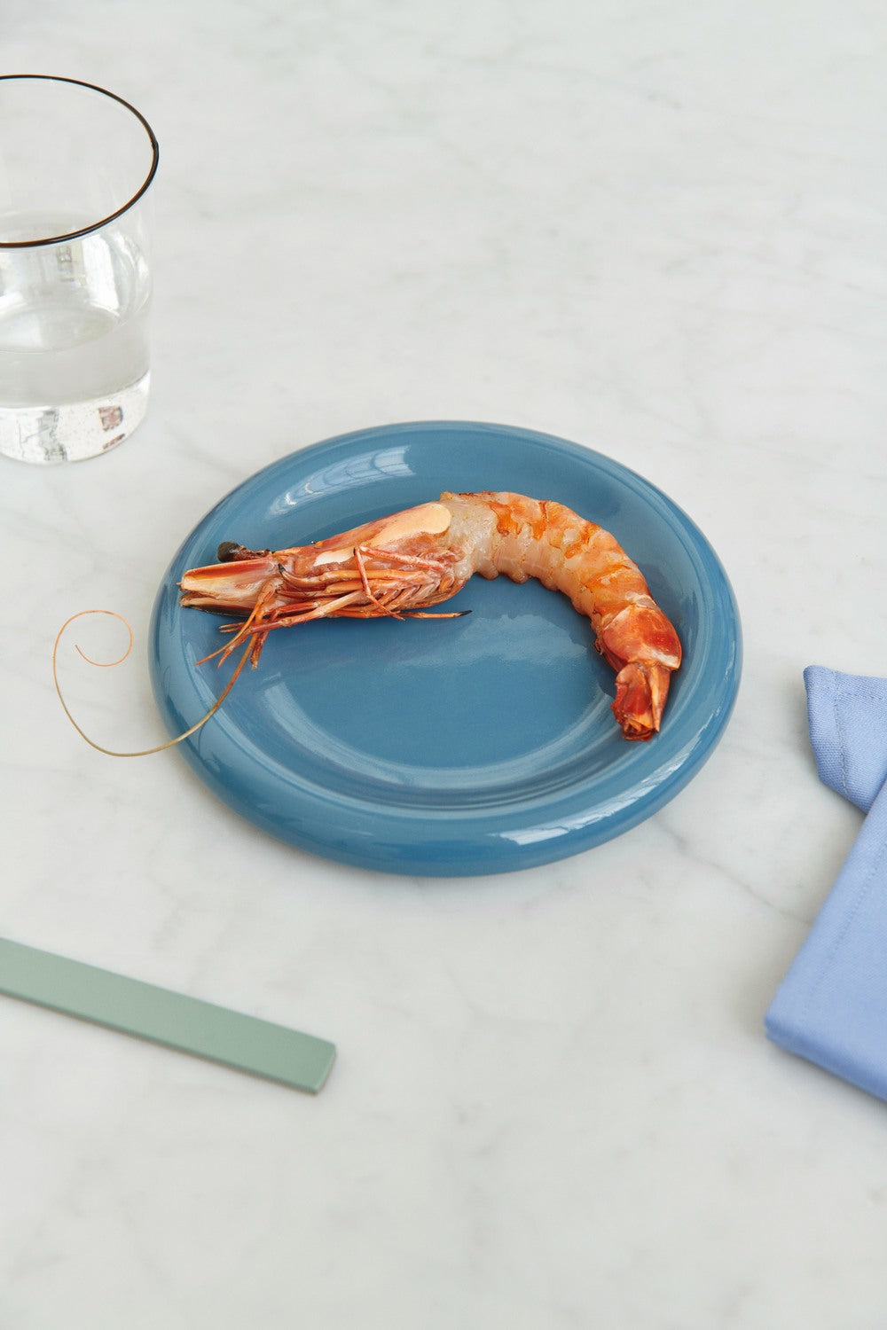 Shrimp on a blue plate with a glass of water and a napkin on a light gray background