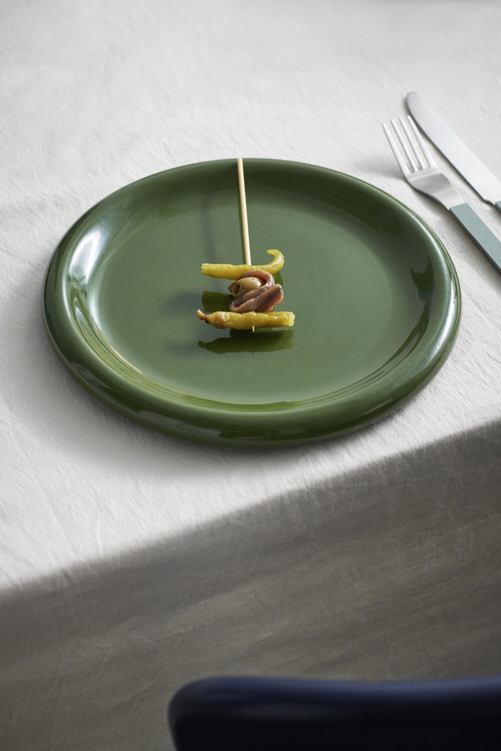 Green plate with skewered food on a white tablecloth