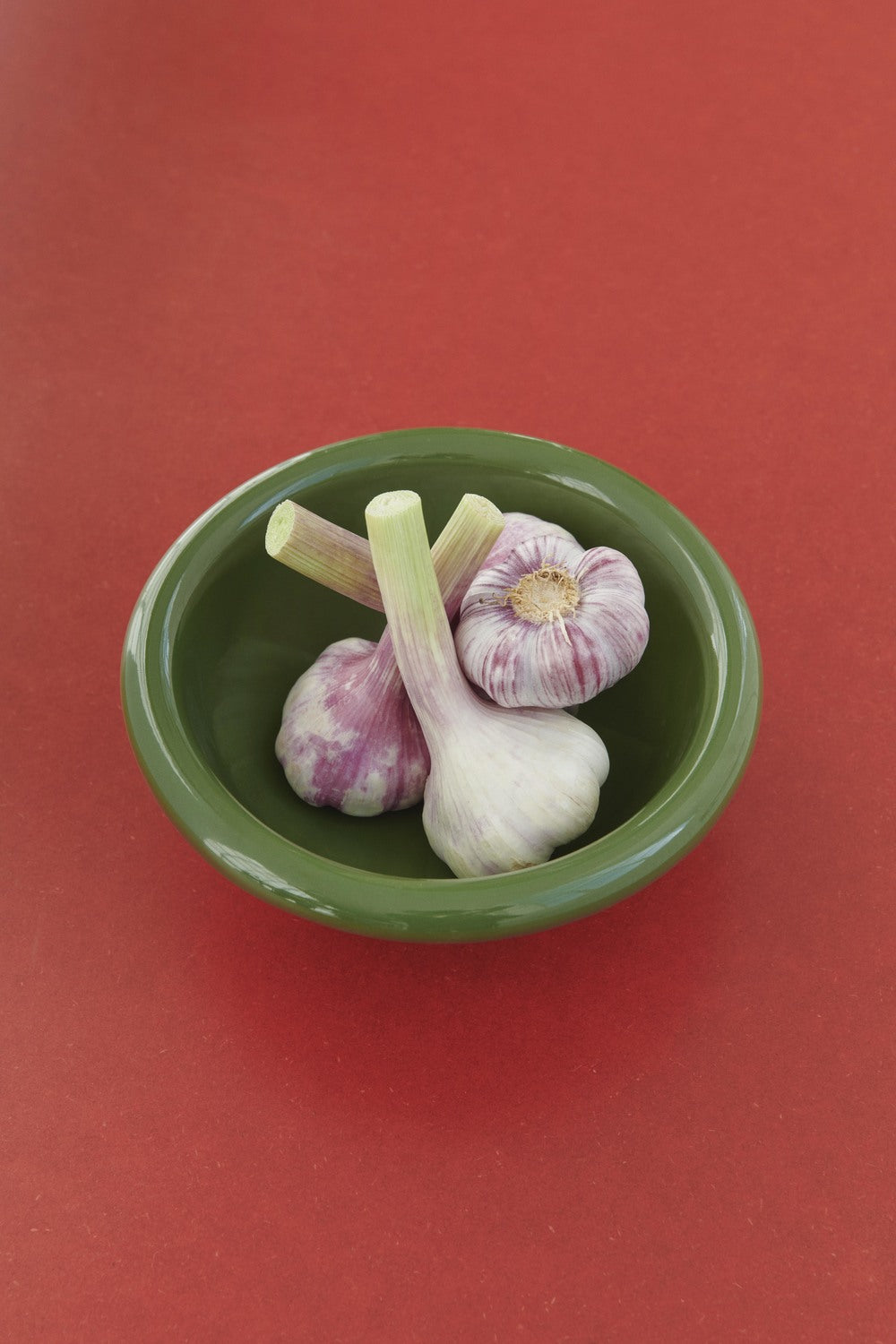 Garlic bulbs in a green bowl on a red background