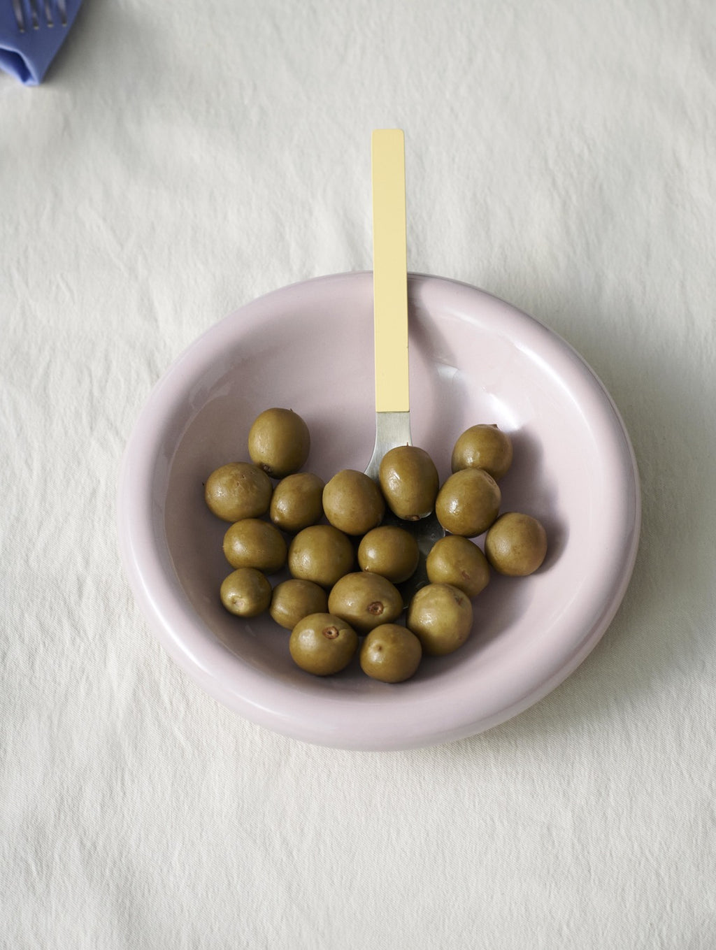 Pink bowl with green olives and a yellow-handled fork on a white background