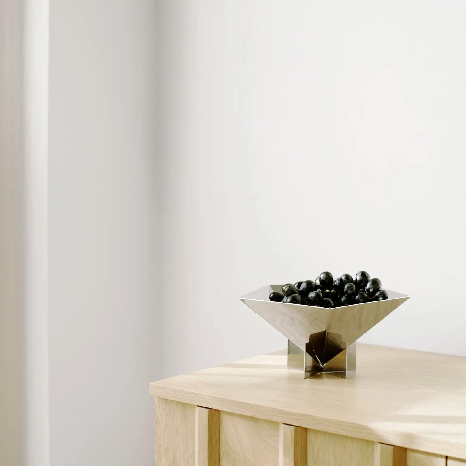 Bowl with black objects on a light wooden table against a white wall