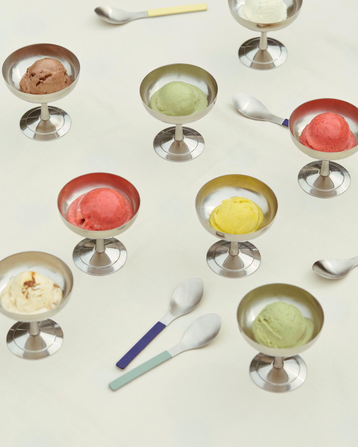 Assorted ice cream flavors in metal dessert cups with spoons on a light background