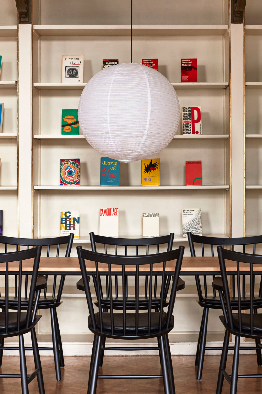 Paper lampshade hanging above dining table surrounded by black spindle chairs
