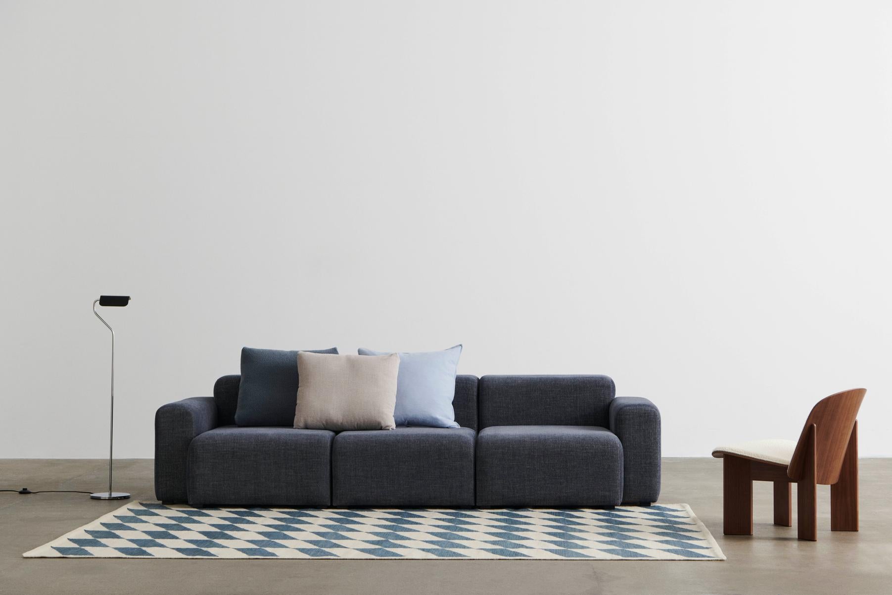 Gray sofa with cushions on a patterned rug in a minimalistic room.
