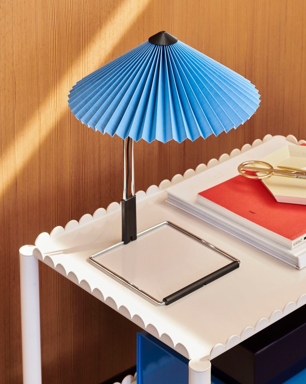Blue pleated lamp on a white table with a wooden wall background