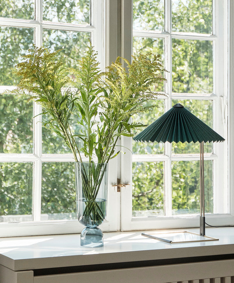 Vase with greenery on a windowsill with a lamp in the foreground