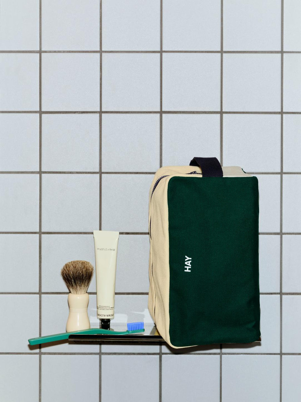 Green and beige travel bag with toiletries on a tiled wall background