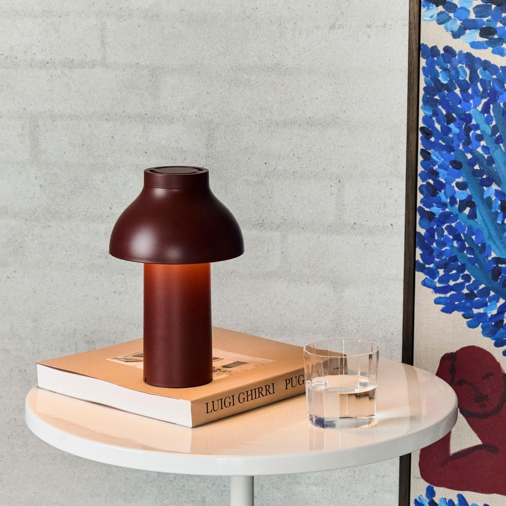 Brown table lamp on a round wooden table with a glass of water and a book against a gray wall.