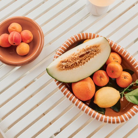 Fruit bowl with melon, oranges, and lemons on a white slatted surface.