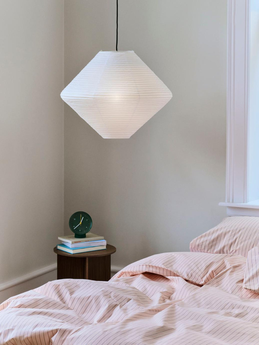 Geometric pendant light in a bedroom with soft bedding and a small table.