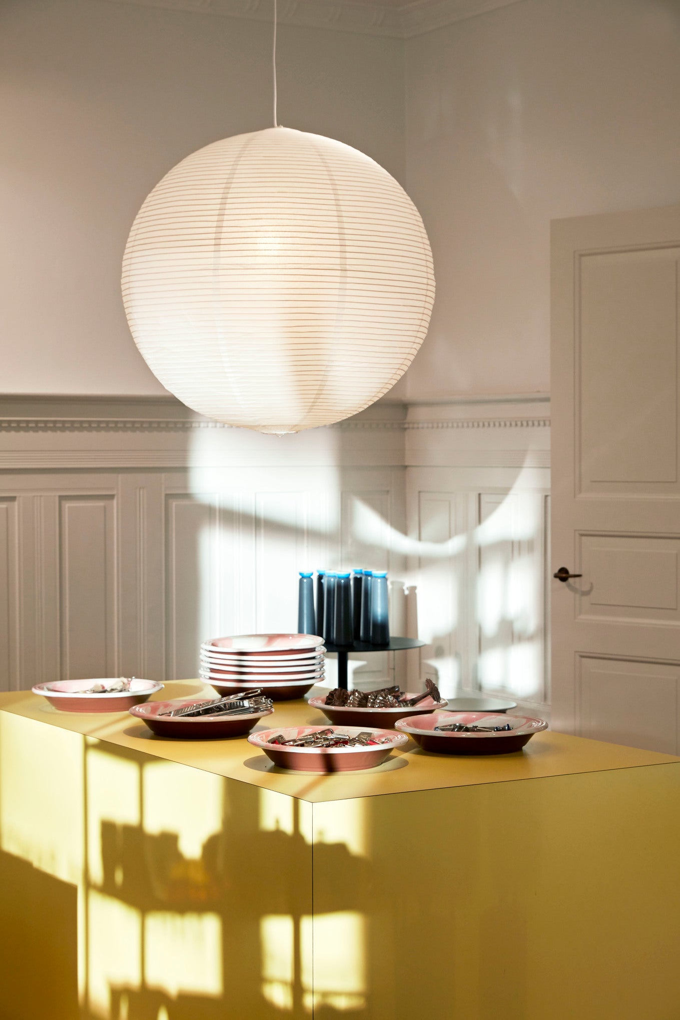 Modern kitchen with a yellow island, pendant light, and decorative items.