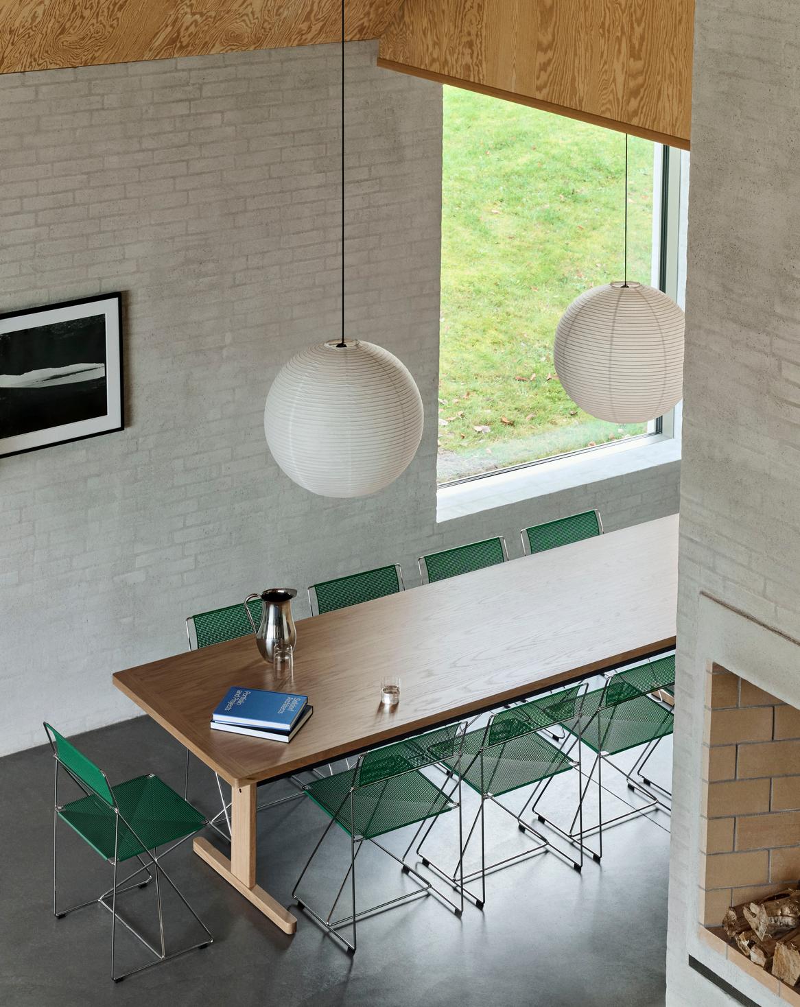 Modern dining area with wooden table and green chairs near a window with a view of grass.