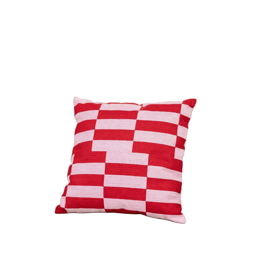 Red and pink checkered pillow on a beige couch with a plant and green blanket in the background.