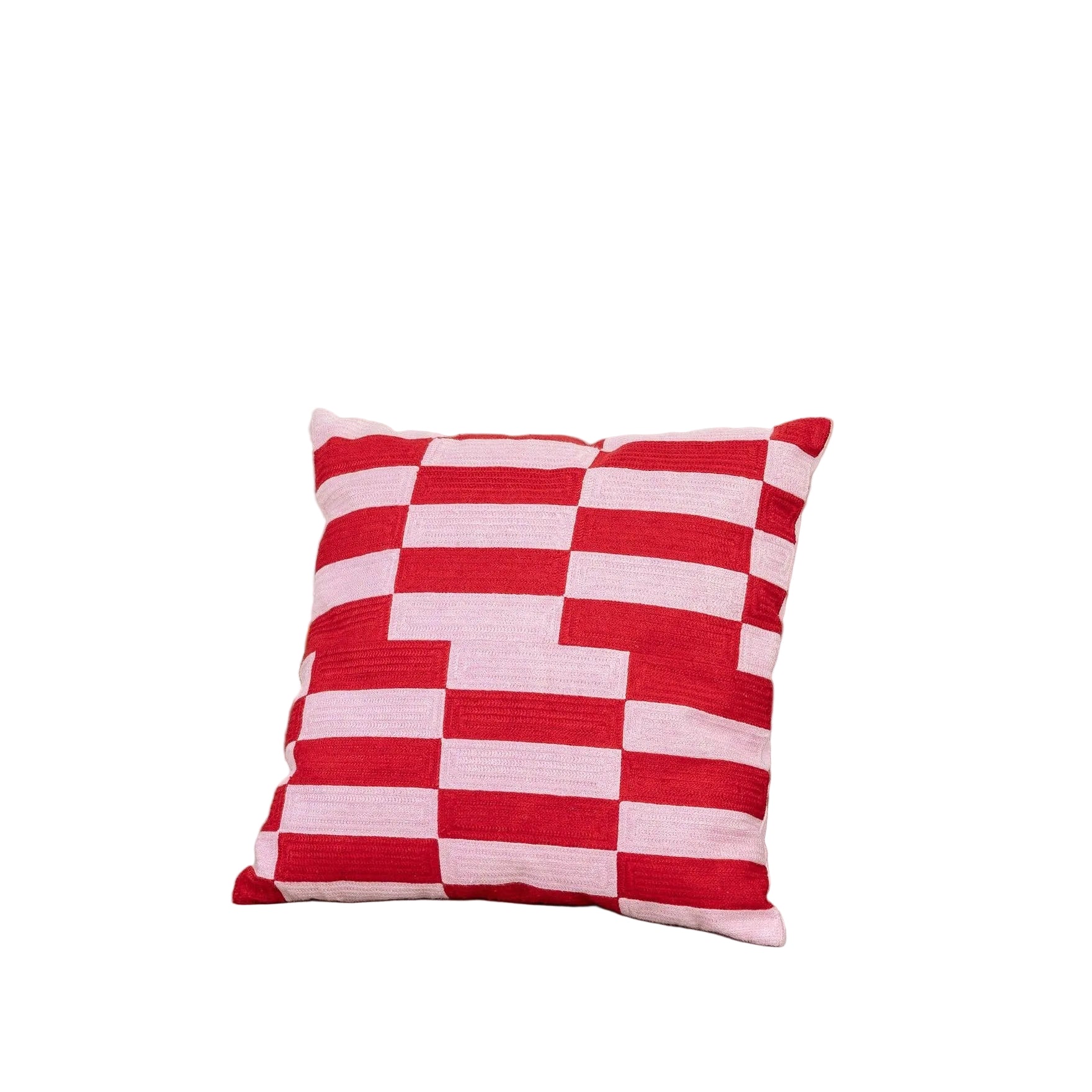 Red and pink checkered pillow on a beige couch with a plant and green blanket in the background.