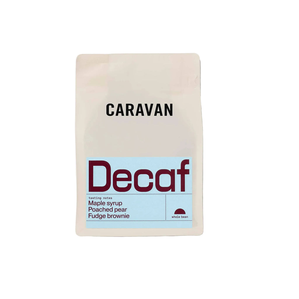 A stand-up pouch of Caravan Decaf coffee on a light gray background. The packaging is off-white with a light blue label area and dark red text for 'Decaf', with black text for 'CARAVAN' above.