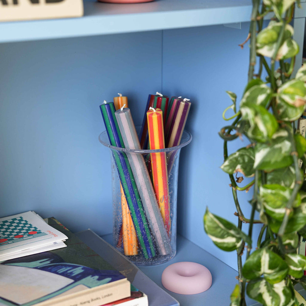 Multicoloured striped candles in a vase against a blue background