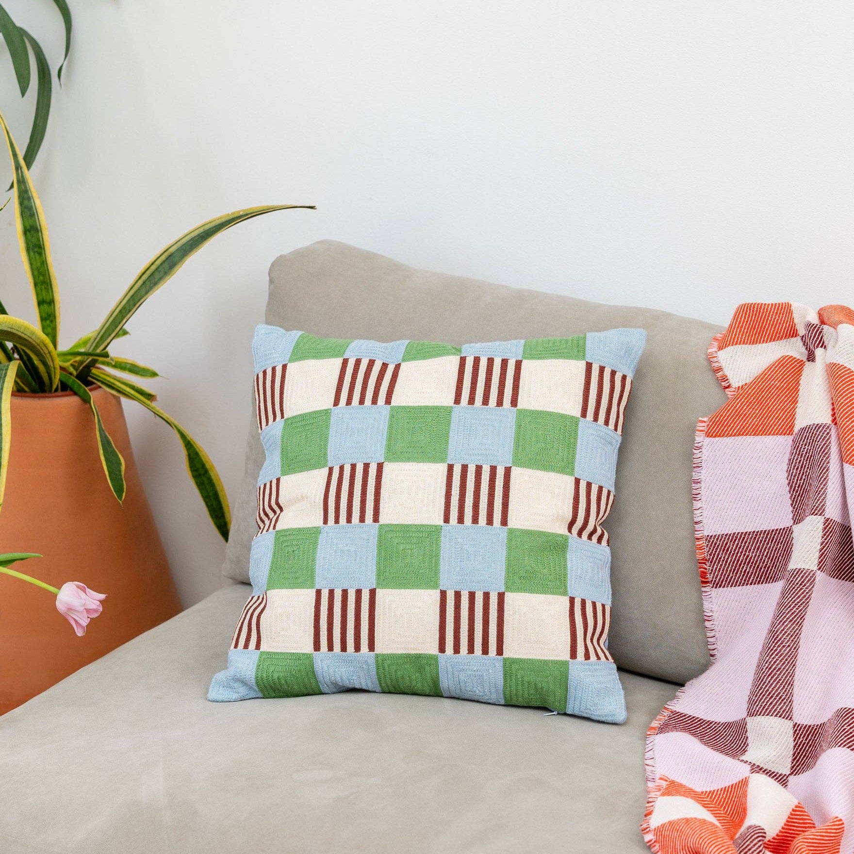 Colorful checkered pillow on a sofa with a plant and plaid blanket in the background