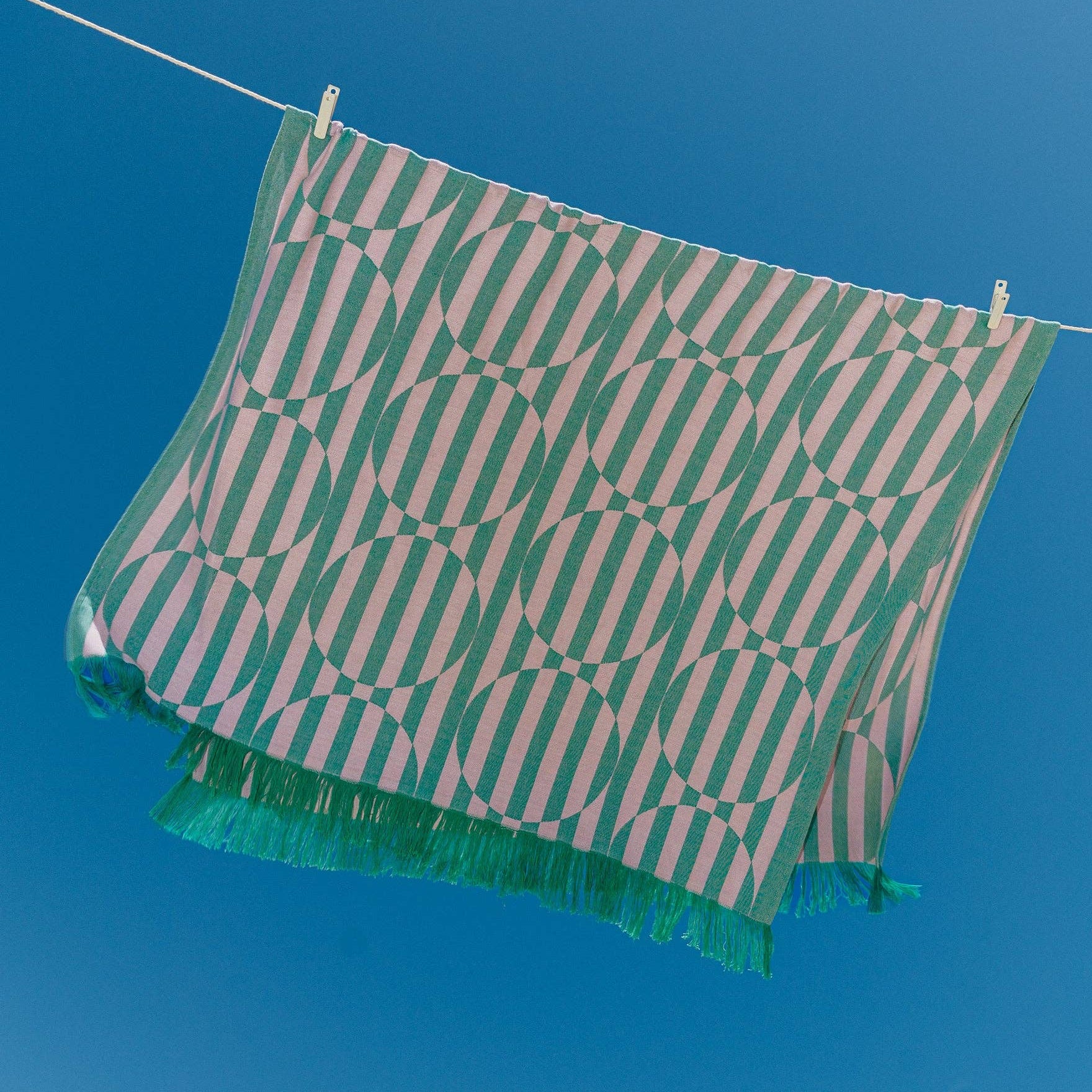 Green and white patterned towel hanging on a clothesline against a blue sky.