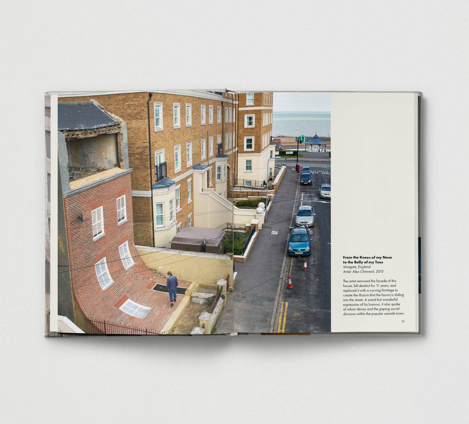 Book with a photograph of a street and buildings on one page and text on the other, on a light gray background.