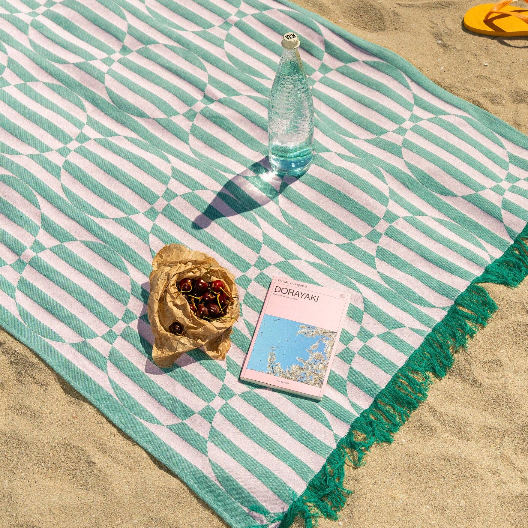 Beach towel with a bottle, shell, and book on sand