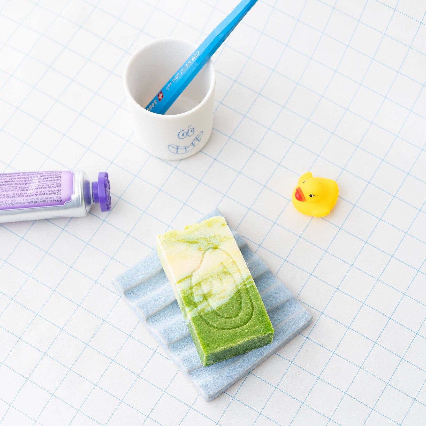 Bar of soap on a blue soap dish with a toothbrush, cup, and rubber duck on a checkered background