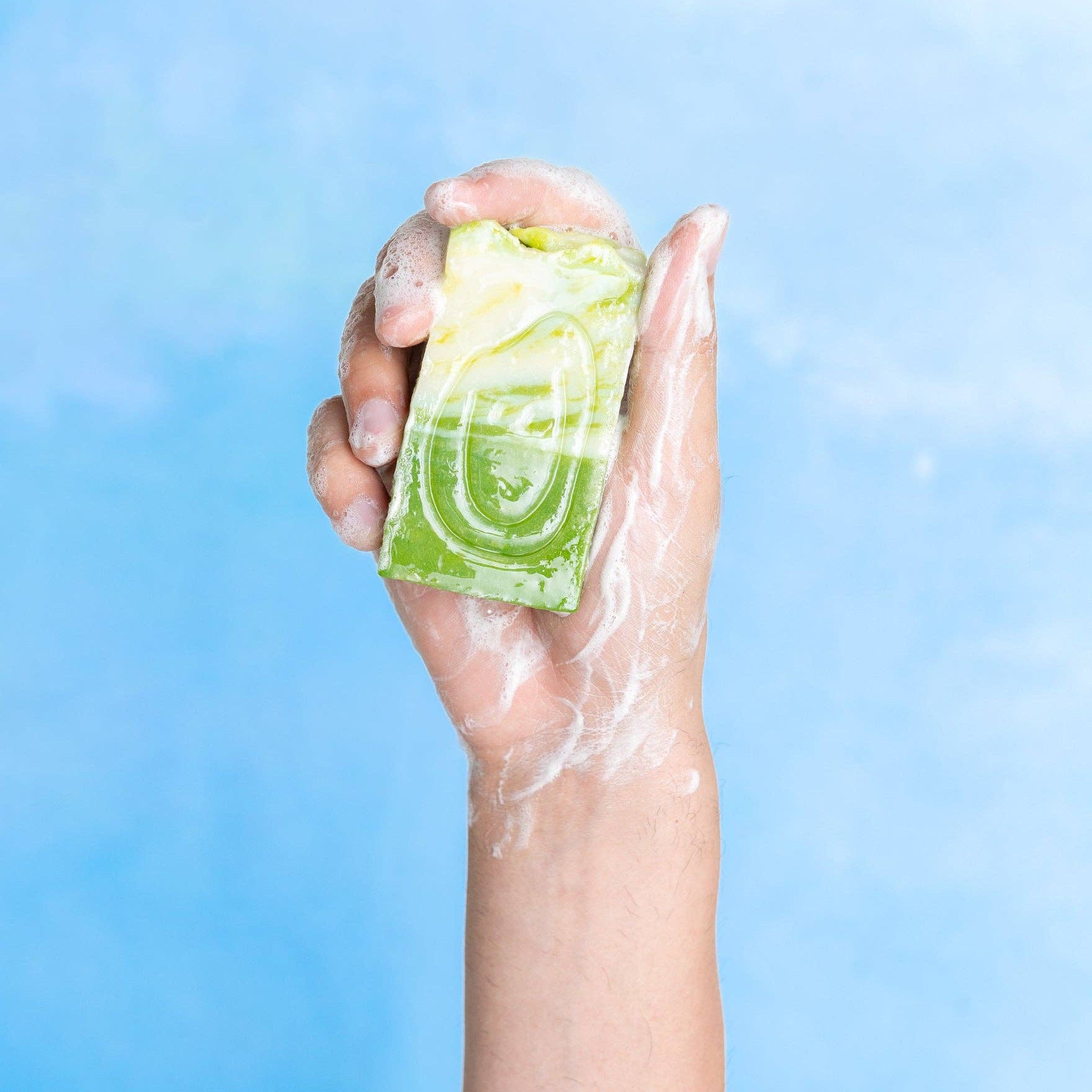 Hand holding a green bar of soap against a blue background