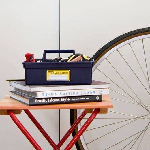 Storage caddy with tools on books next to a bicycle wheel