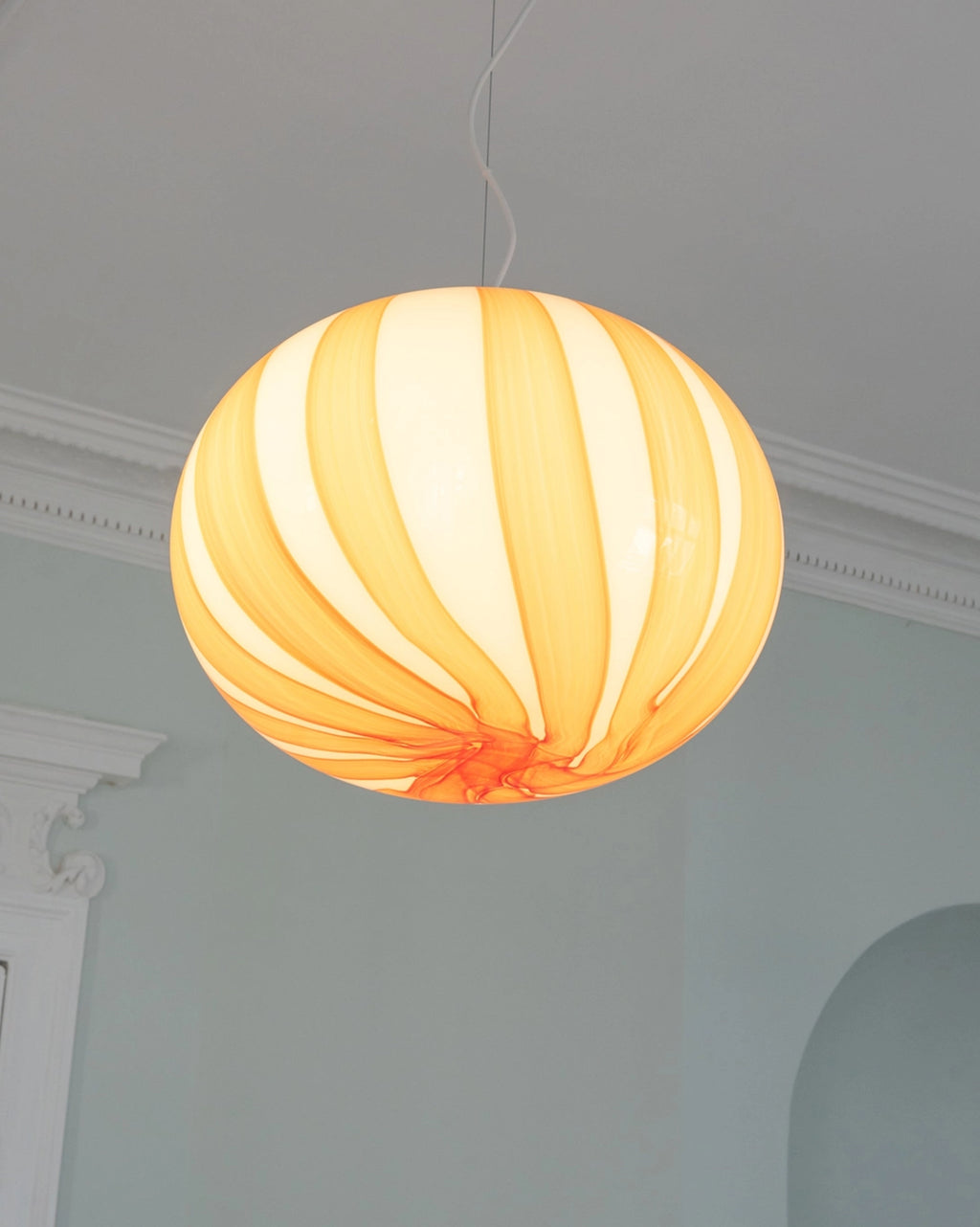 Spherical pendant light with orange and white stripes hanging against a neutral wall.